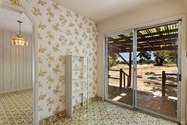 doorway with wallpapered walls and a textured ceiling