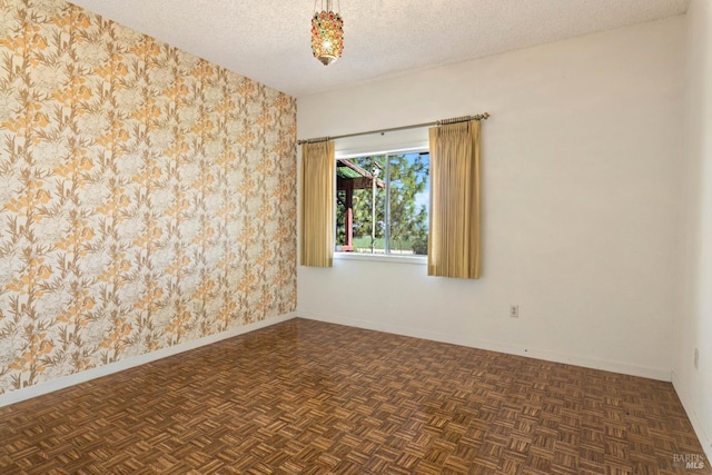 empty room with wallpapered walls, parquet flooring, baseboards, and a textured ceiling