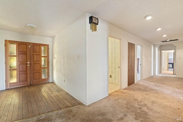 hall featuring a textured ceiling, visible vents, and light colored carpet