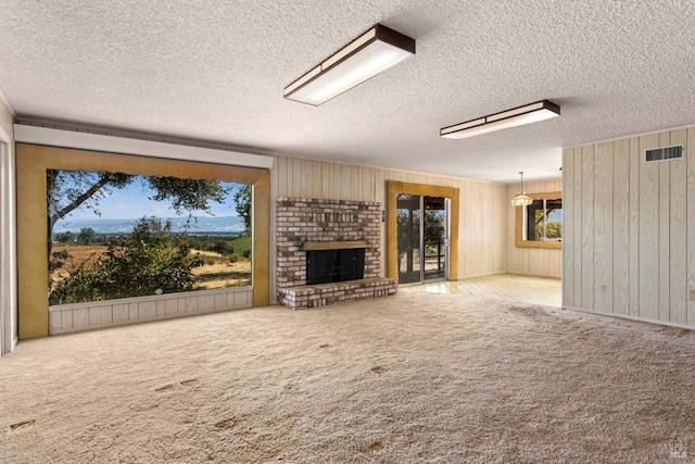 unfurnished living room with carpet, a brick fireplace, visible vents, and wood walls