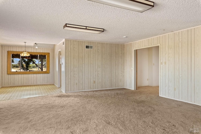 spare room with a textured ceiling, visible vents, and light colored carpet