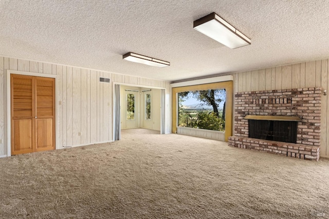 unfurnished living room with carpet, a brick fireplace, wood walls, and a textured ceiling