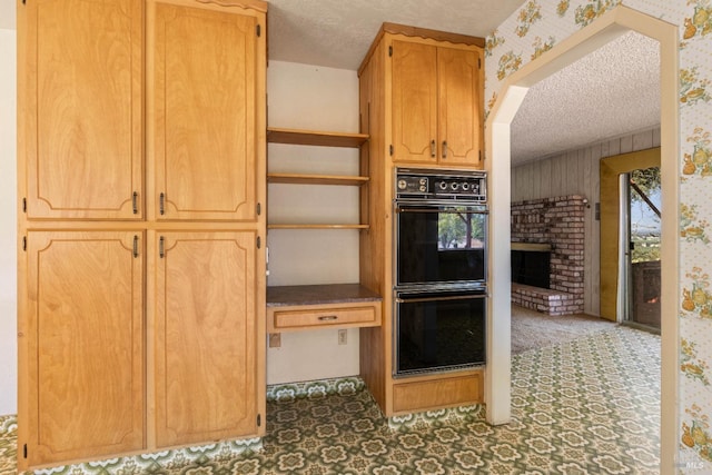 kitchen with a fireplace, dark countertops, dobule oven black, a textured ceiling, and wallpapered walls