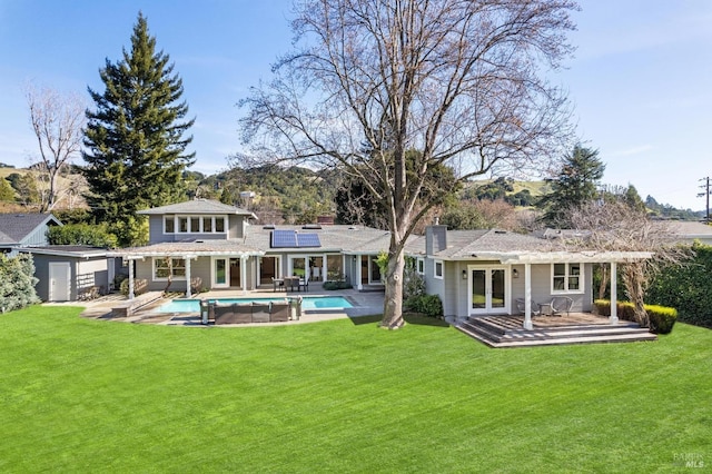 rear view of property with solar panels, an outdoor structure, a lawn, an outdoor pool, and a chimney