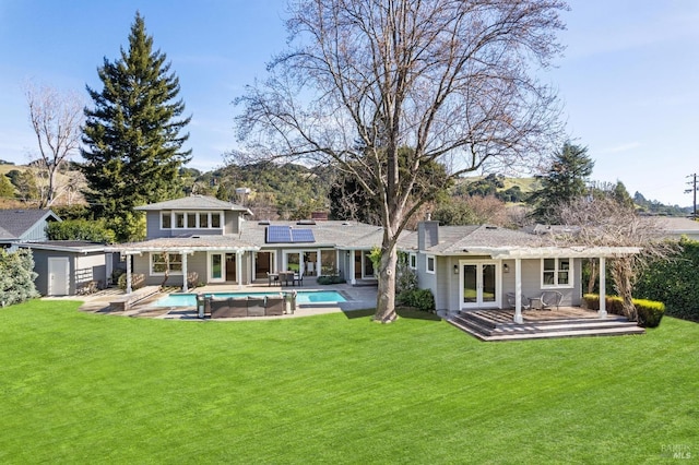 rear view of property with solar panels, an outdoor structure, a lawn, an outdoor pool, and a chimney