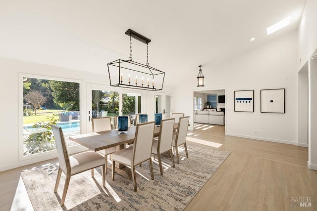 dining room with a chandelier, baseboards, a towering ceiling, and light wood finished floors