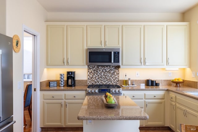 kitchen with stainless steel appliances, light stone counters, a kitchen island, and cream cabinetry