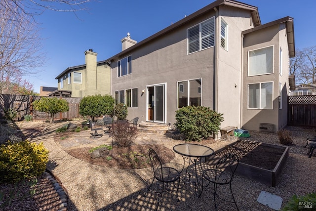 back of property featuring a vegetable garden, a patio, a chimney, stucco siding, and a fenced backyard