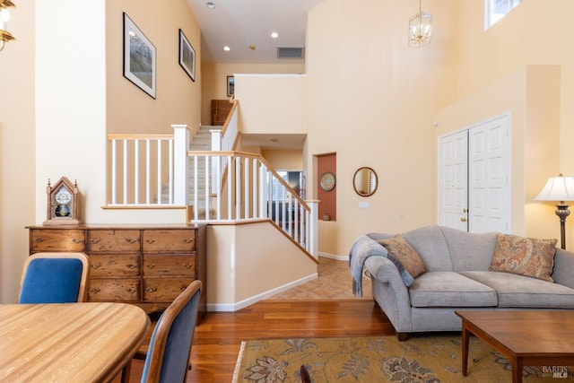 living room featuring visible vents, stairway, wood finished floors, a high ceiling, and a notable chandelier