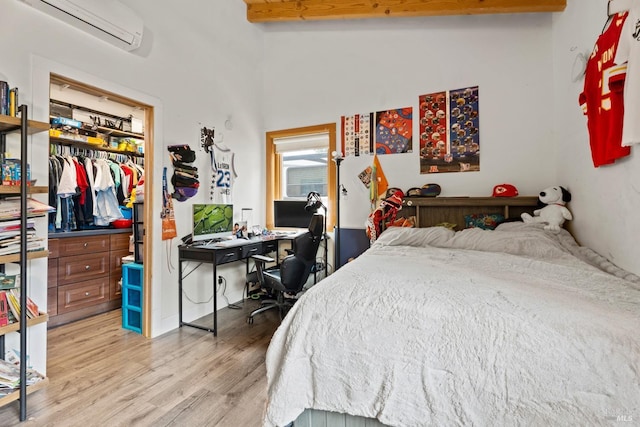 bedroom featuring light wood-style floors, a wall mounted AC, a closet, beam ceiling, and a walk in closet