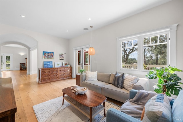 living room featuring a healthy amount of sunlight, light wood finished floors, and arched walkways