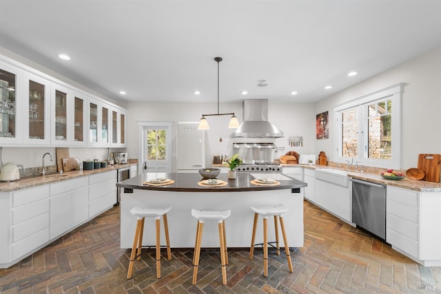 kitchen with wall chimney range hood, white cabinetry, stainless steel dishwasher, and recessed lighting