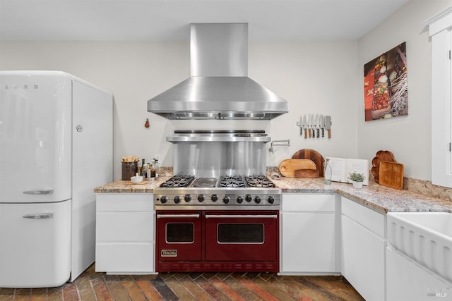 kitchen with light stone counters, exhaust hood, white cabinets, freestanding refrigerator, and double oven range