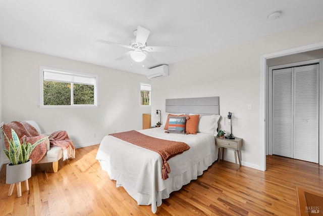 bedroom featuring a ceiling fan, a wall unit AC, light wood-style flooring, and baseboards