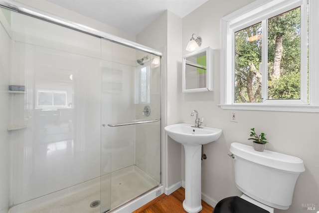 bathroom with a stall shower, baseboards, toilet, wood finished floors, and a sink