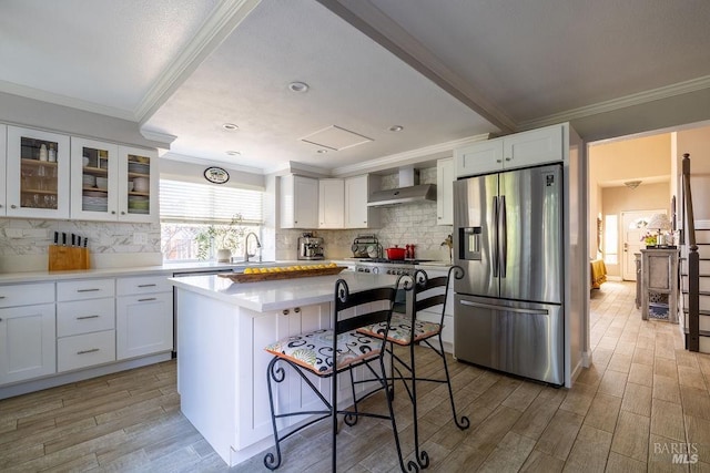 kitchen featuring white cabinets, a breakfast bar area, wood tiled floor, stainless steel appliances, and wall chimney range hood