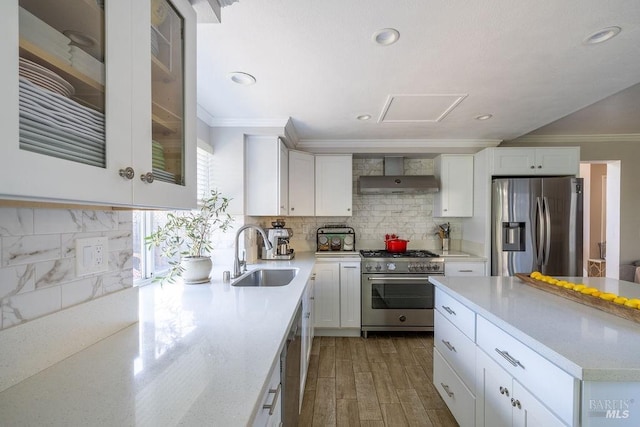 kitchen with white cabinets, wall chimney exhaust hood, stainless steel appliances, crown molding, and a sink