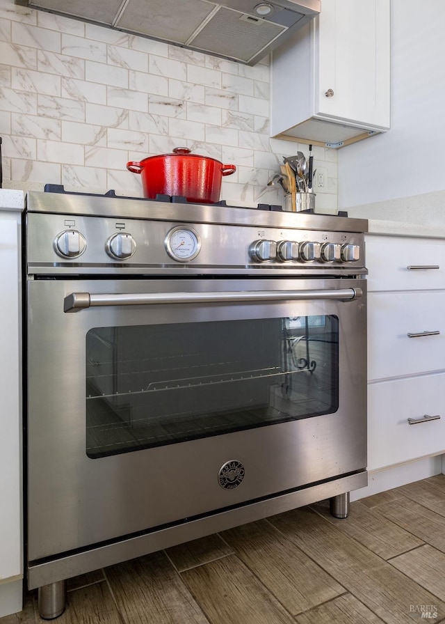 interior details with tasteful backsplash, stainless steel stove, light countertops, and white cabinets