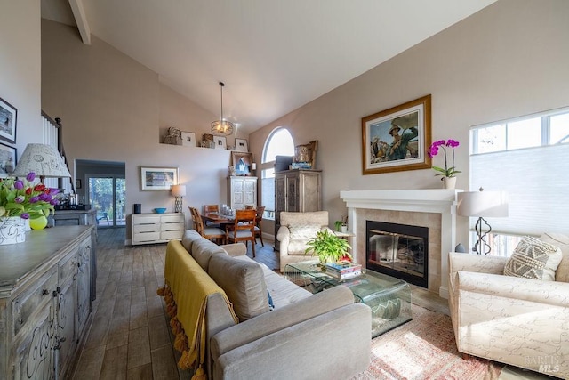 living area with high vaulted ceiling, a tile fireplace, and dark wood finished floors