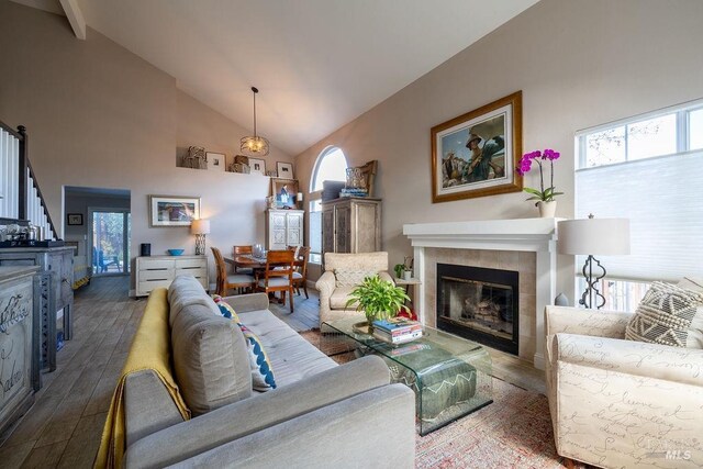 living area featuring high vaulted ceiling, dark wood-style flooring, and a tiled fireplace