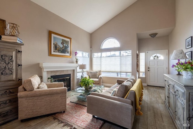 living room featuring baseboards, high vaulted ceiling, wood finished floors, and a tile fireplace