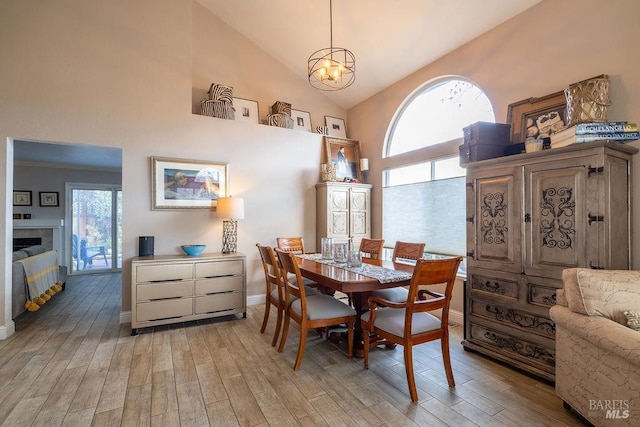 dining space with high vaulted ceiling, a tile fireplace, a notable chandelier, and light wood finished floors