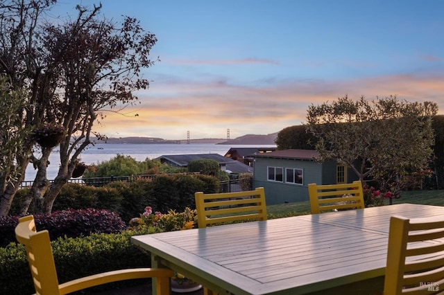 deck at dusk featuring a water view and fence