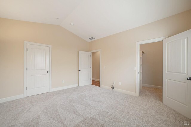 unfurnished bedroom featuring a closet, light colored carpet, visible vents, vaulted ceiling, and baseboards