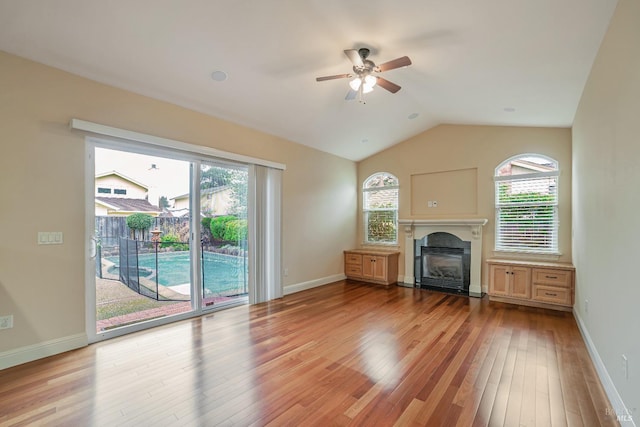 unfurnished living room featuring vaulted ceiling, a glass covered fireplace, light wood-style flooring, and baseboards