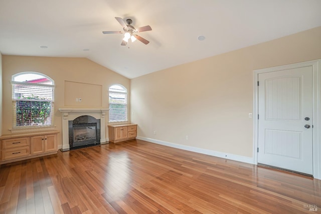 unfurnished living room with plenty of natural light, light wood-type flooring, a glass covered fireplace, and lofted ceiling