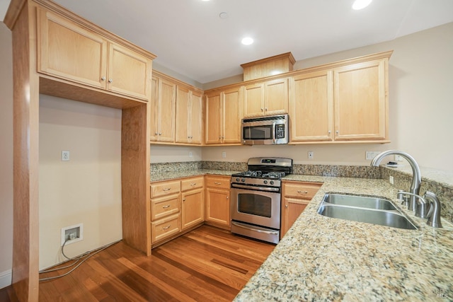 kitchen featuring wood finished floors, light stone countertops, stainless steel appliances, light brown cabinets, and a sink