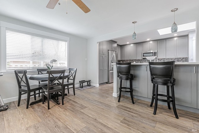 kitchen with pendant lighting, gray cabinets, light countertops, appliances with stainless steel finishes, and a kitchen bar