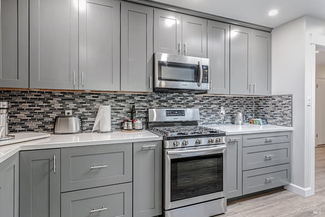 kitchen with decorative backsplash, appliances with stainless steel finishes, light countertops, gray cabinetry, and light wood-style floors