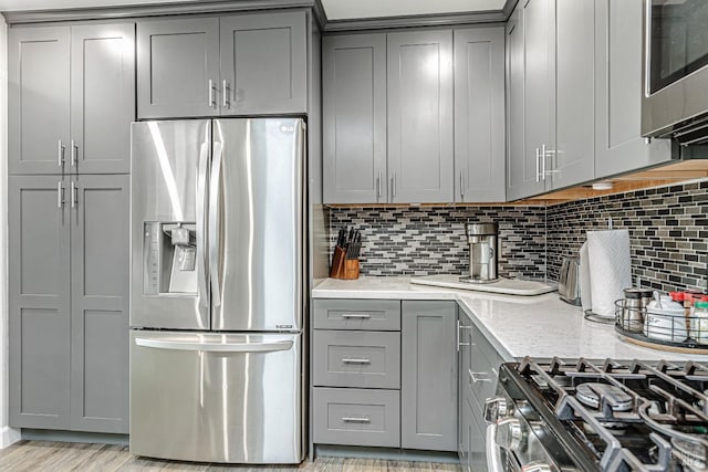 kitchen with decorative backsplash, appliances with stainless steel finishes, gray cabinets, and light stone counters