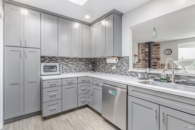 kitchen featuring dishwasher, light countertops, gray cabinetry, light wood-style floors, and a sink