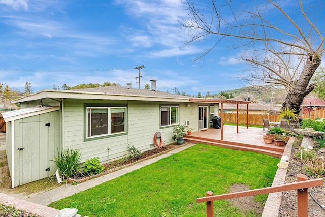 rear view of house featuring a lawn, fence, a shed, an outdoor structure, and a wooden deck