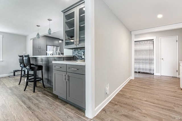 kitchen featuring hanging light fixtures, glass insert cabinets, light countertops, and gray cabinetry