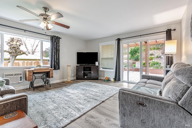 living room featuring a ceiling fan, an AC wall unit, baseboards, and wood finished floors