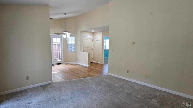 carpeted spare room featuring high vaulted ceiling, baseboards, and a ceiling fan