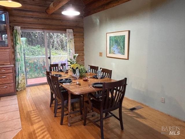 dining room featuring light wood finished floors, beamed ceiling, rustic walls, and visible vents