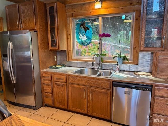 kitchen with brown cabinetry, glass insert cabinets, stainless steel appliances, light countertops, and a sink