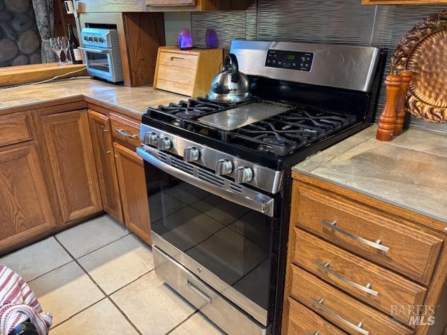 kitchen with tile countertops, gas range, brown cabinets, and light tile patterned flooring