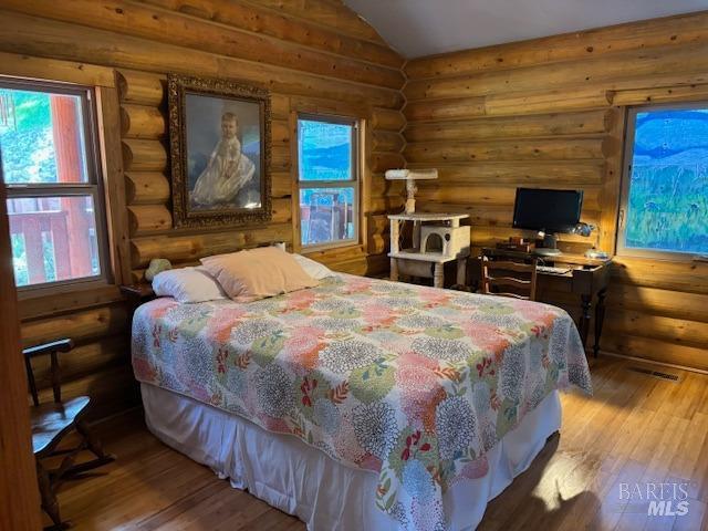 bedroom featuring lofted ceiling, rustic walls, and wood finished floors