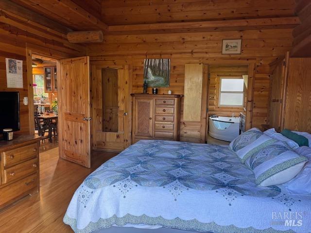 bedroom with rustic walls, a wall unit AC, and wood finished floors