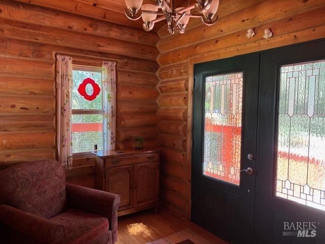 doorway with an inviting chandelier, light wood-style flooring, log walls, and french doors