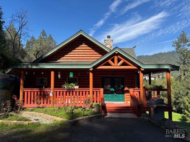 log cabin with covered porch, a chimney, and log veneer siding