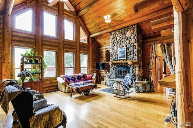 living area with a stone fireplace, wooden ceiling, rustic walls, a ceiling fan, and wood-type flooring