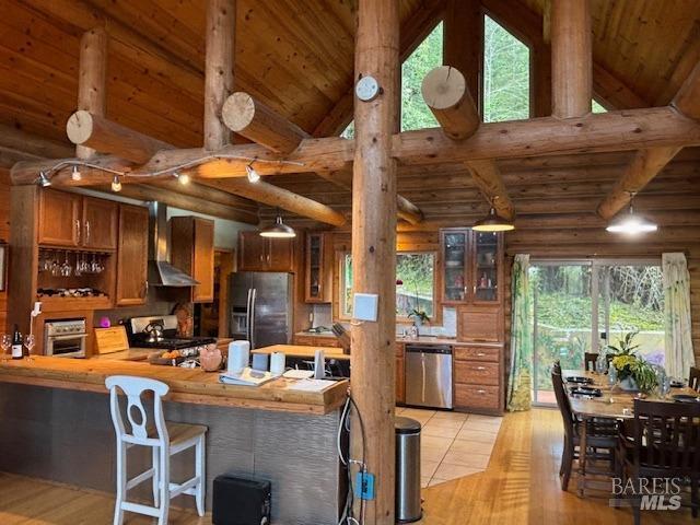 kitchen featuring brown cabinetry, fridge with ice dispenser, wall chimney range hood, range, and dishwasher