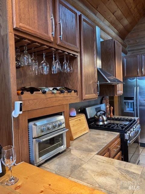 kitchen with stainless steel gas stove, tile patterned floors, vaulted ceiling, ventilation hood, and light countertops