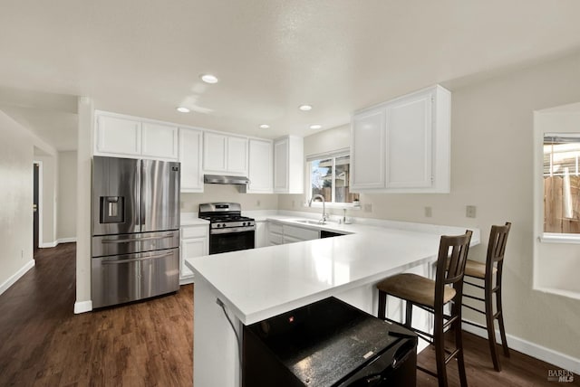 kitchen with under cabinet range hood, a peninsula, a sink, light countertops, and appliances with stainless steel finishes